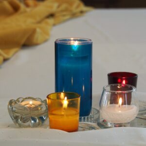 Five colorful candles lit on white linen, creating a warm and serene atmosphere.